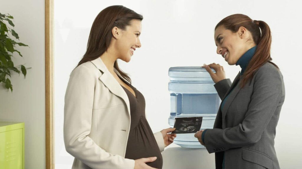 a pregnant woman talking to another woman and showing baby ultrasound picture