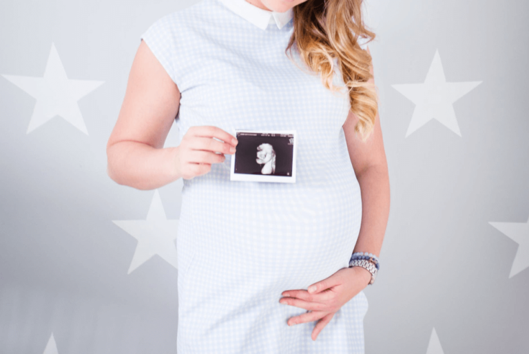 Pregnant woman holding her belly and a picture of her ultrasound.