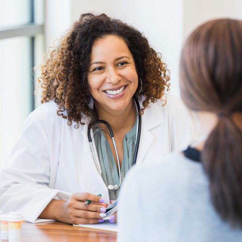 A smiling mid adult female doctor listens as a female patient discusses her health.