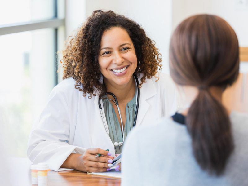 A smiling mid adult female doctor listens as a female patient discusses her health.